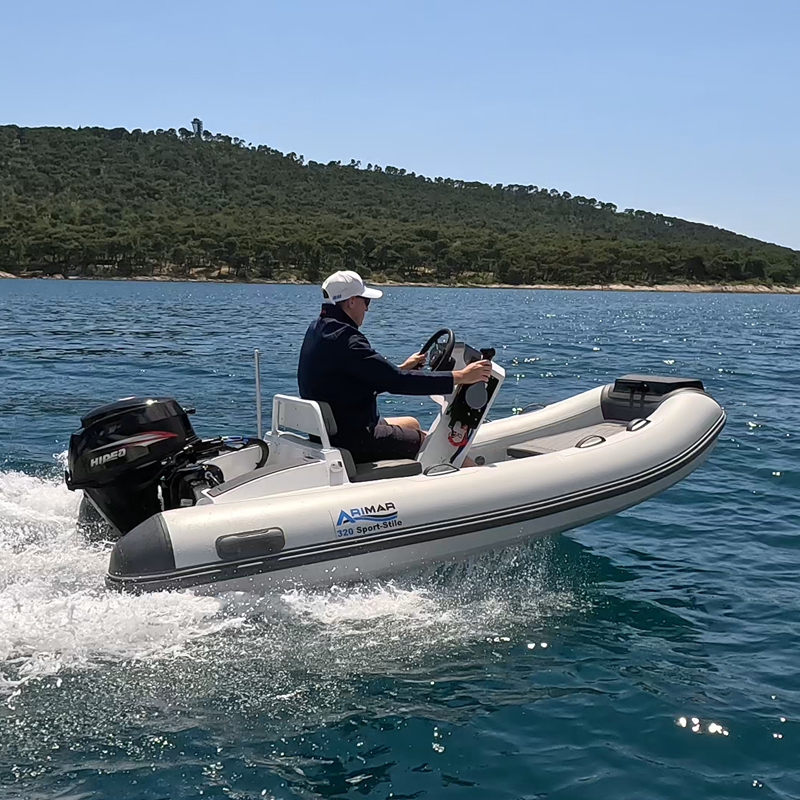 Gommone bianco in navigazione, uomo alla guida su mare calmo con vegetazione sullo sfondo.